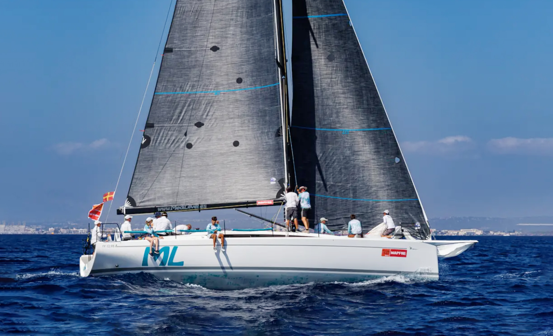 Side view of the Italia Yachts IY 12.98 Fuoriserie sailing yacht underway with black racing sails and crew on deck.